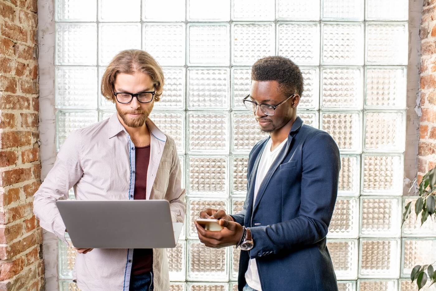 Two professionals collaborating in a modern office, one using a laptop and the other checking a smartphone, representing AI-driven solutions for customer support and sales efficiency.